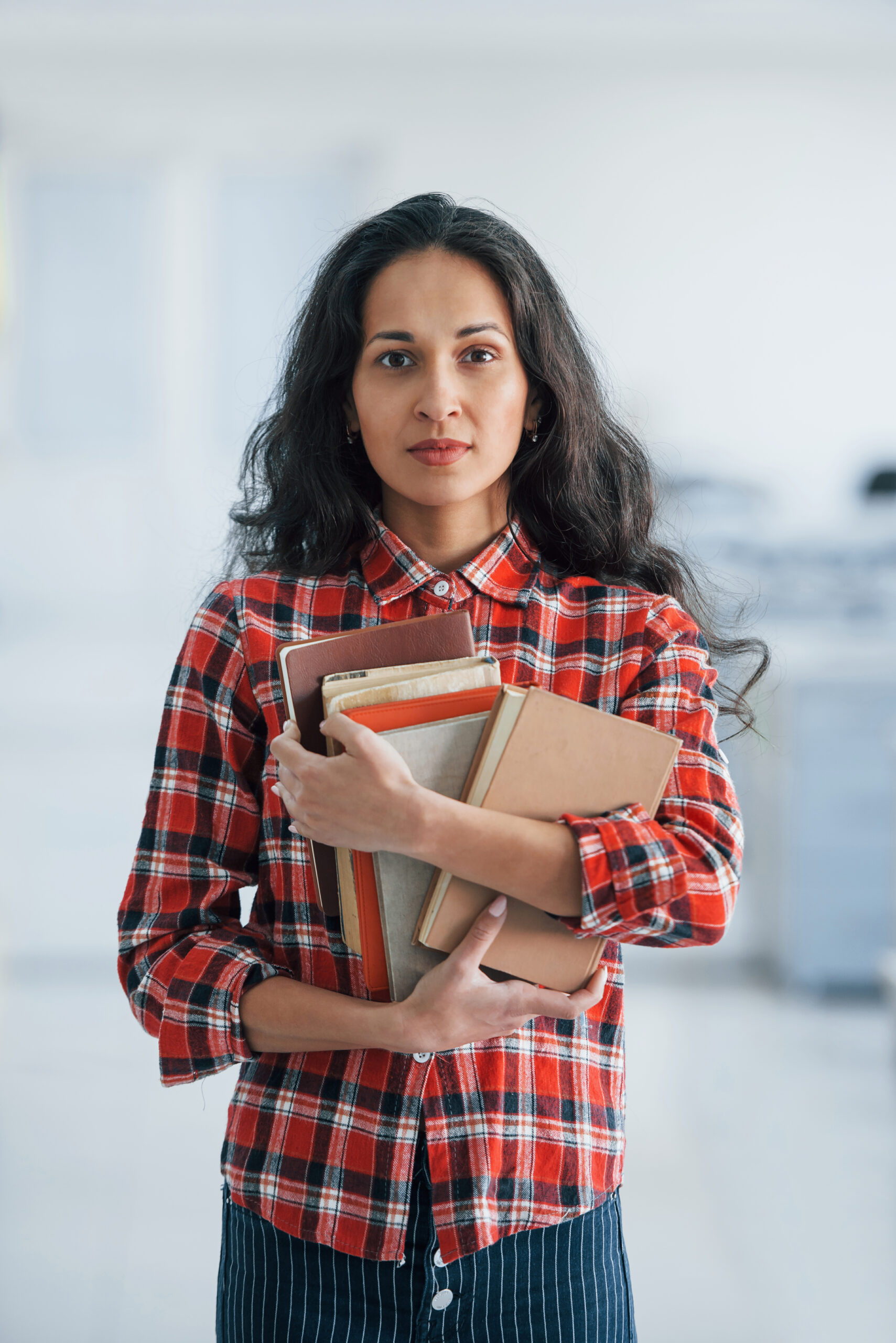 Vertical photo of attractive young woman standing in the office and holding books and documents.